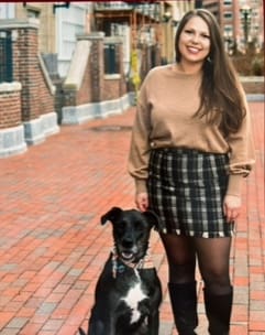 A woman in a skirt and boots with her dog.