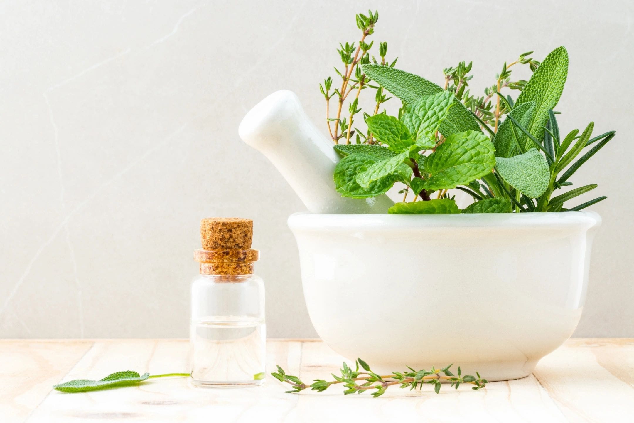 A mortar and pestle with herbs in it next to a bottle of essential oil.